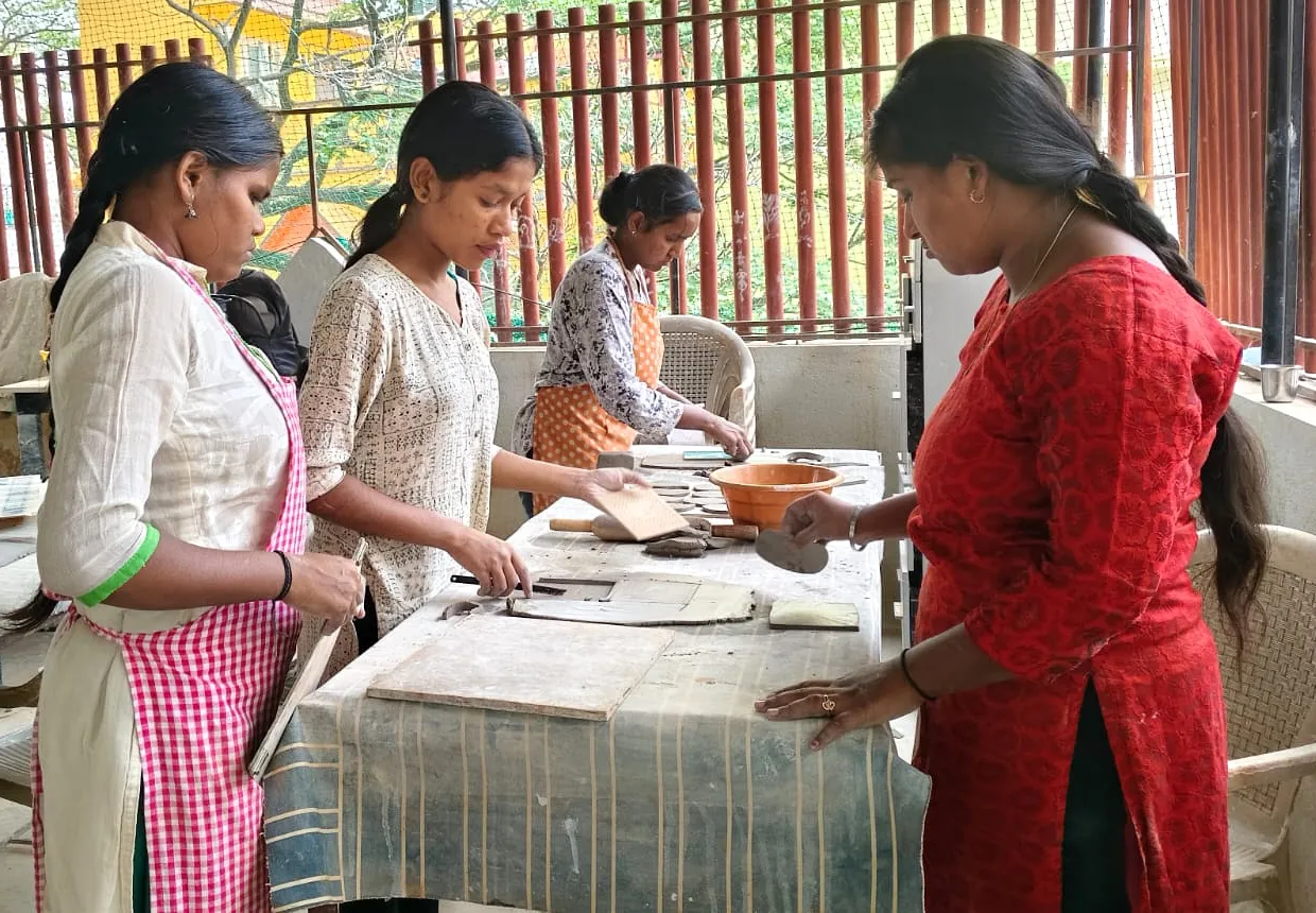 Trainees shape clay slabs by hand around a shared worktable at the Asmishilp studio