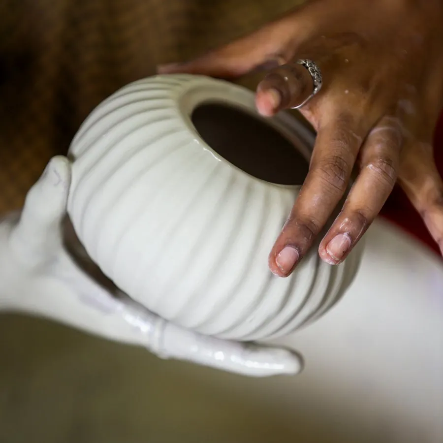 Hands finishing a fluted white ceramic pot