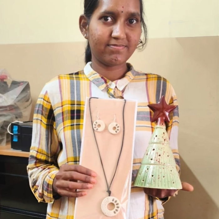 A young woman holds up handmade ceramic jewellery, a pendant and earrings on a card, and a small green ceramic Christmas tree.